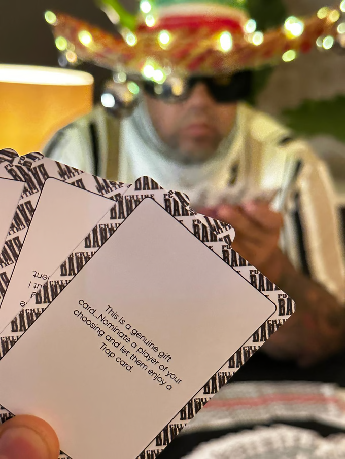 Person holding playing cards with text, wearing a sombrero and sunglasses.